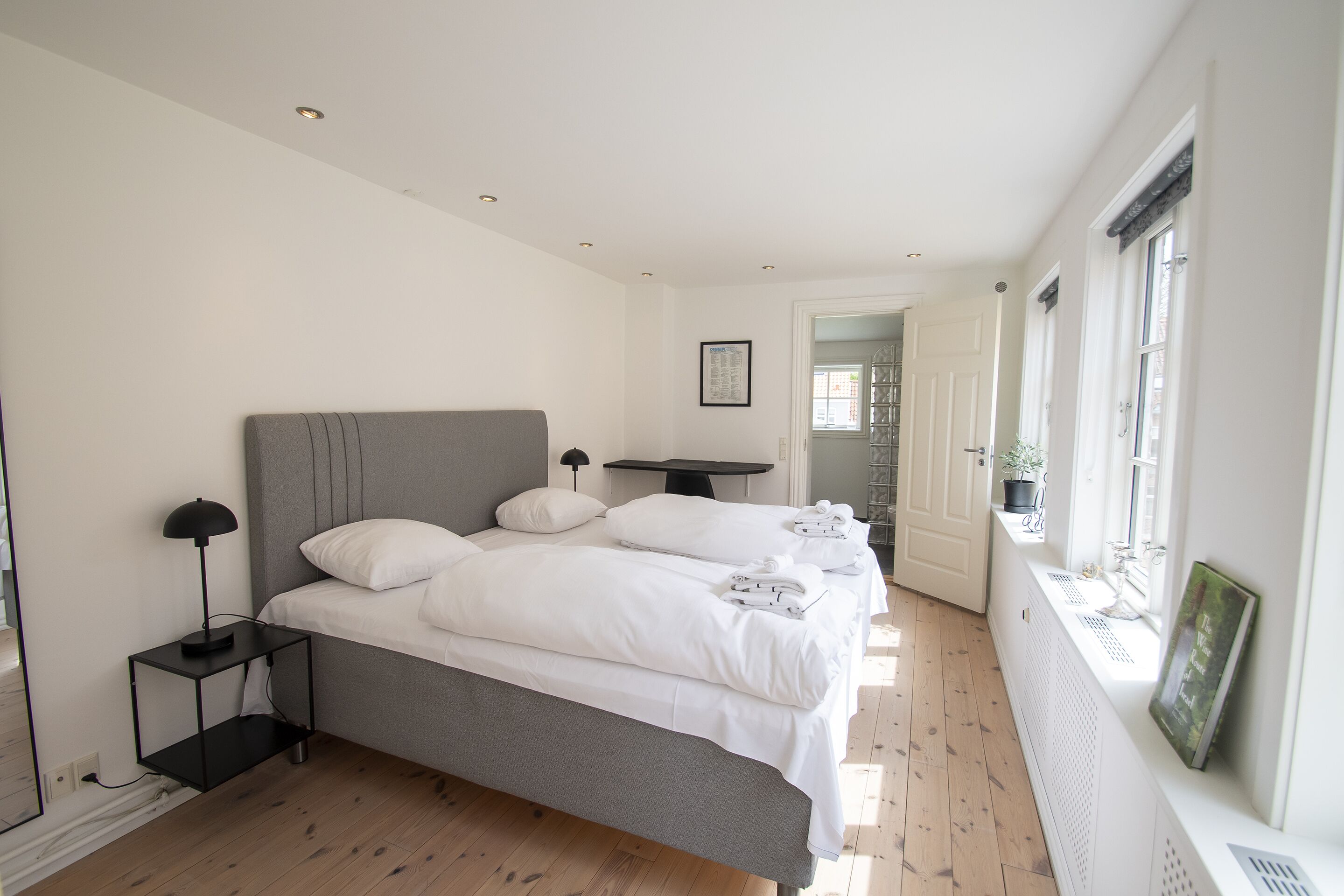 A modern bedroom with a large bed, bedside tables, a small table, and a window with a view.