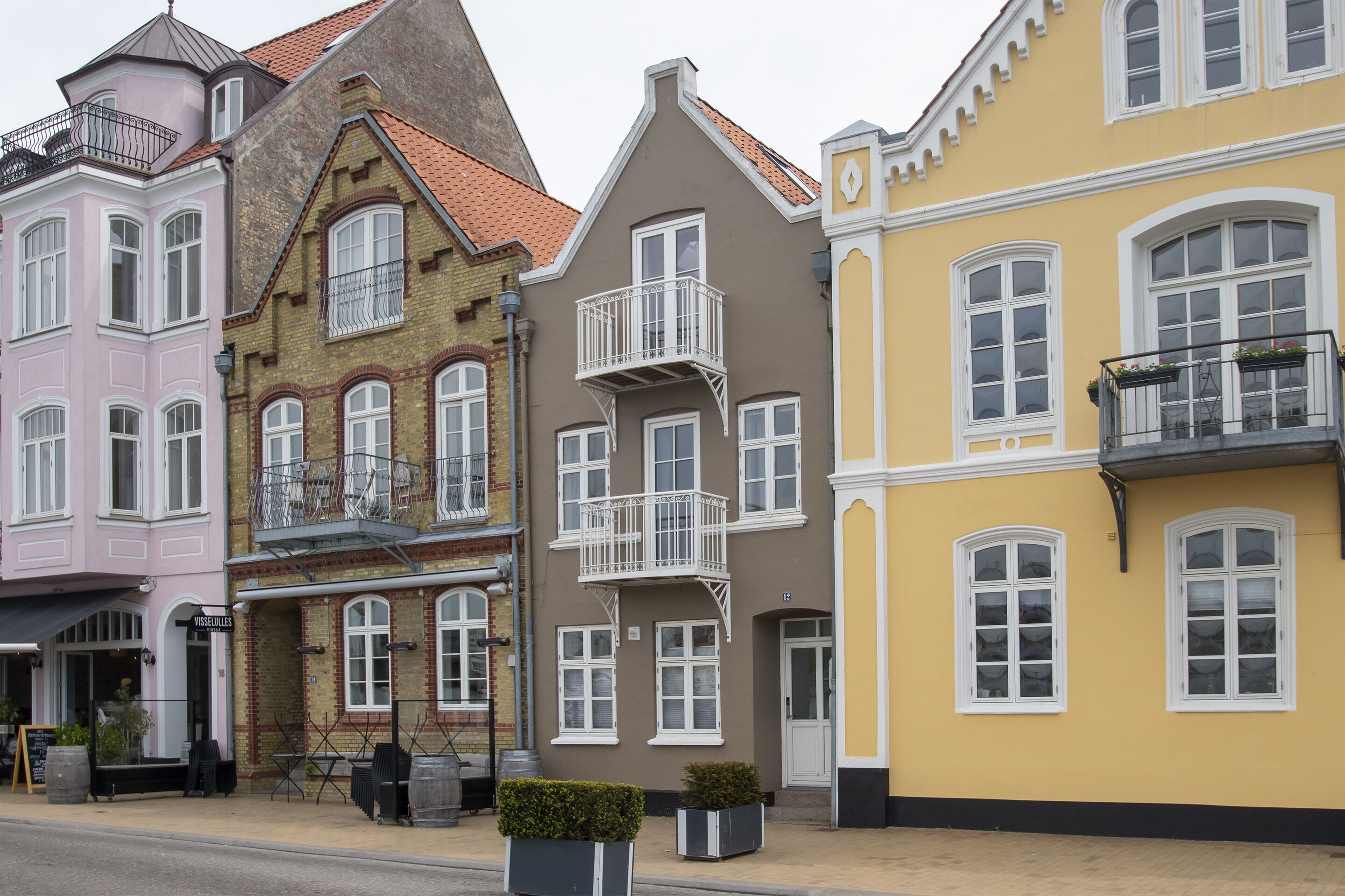 Eine Reihe bunter Gebäude mit unterschiedlichen Baustilen, darunter ein rosafarbenes Gebäude mit Balkon und ein gelbes Gebäude mit weißem Fensterrahmen.