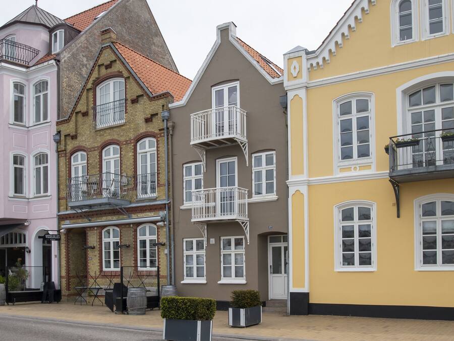 Eine Reihe bunter Gebäude mit unterschiedlichen Baustilen, darunter ein rosafarbenes Gebäude mit Balkon und ein gelbes Gebäude mit weißem Fensterrahmen.