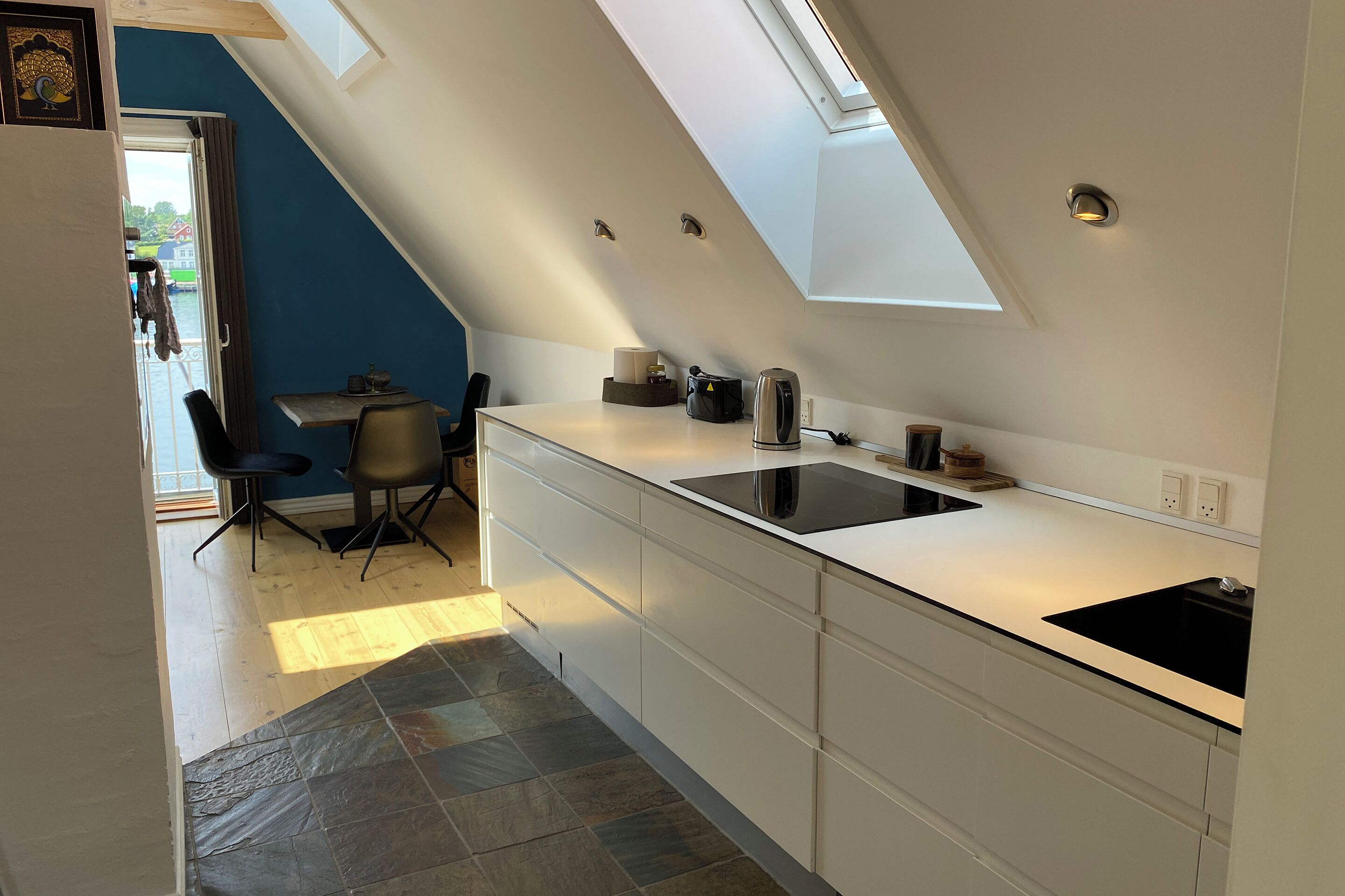 A modern kitchen with a skylight, white cabinets, a black sink, and a dining area with chairs.