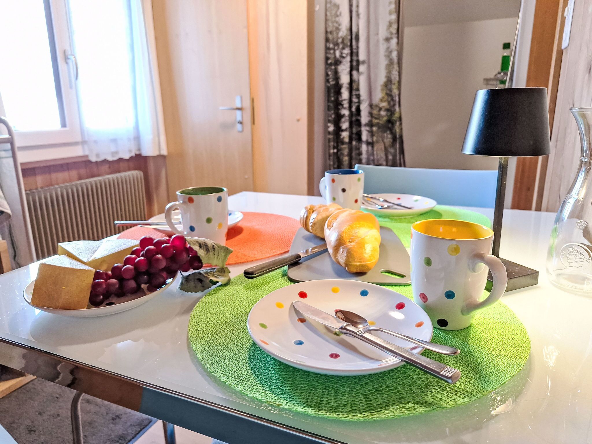 A breakfast table with a croissant, grapes, cheese, and a mug.