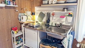 A compact kitchen with a sink, a small refrigerator, and a stove. There are shelves with various kitchen items and a coffee maker.