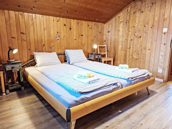 A wooden-paneled bedroom with a double bed, two bedside tables, a lamp, and a chair.