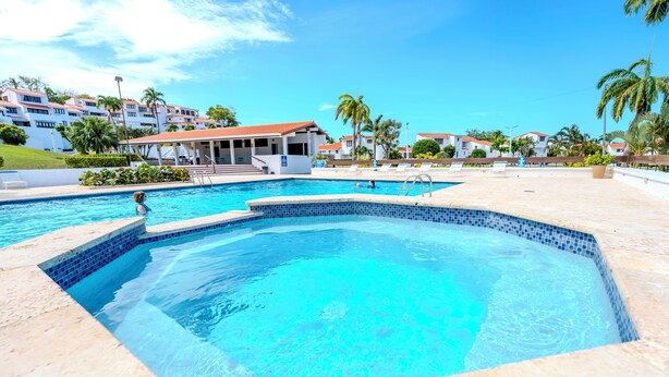 A swimming pool with a tiled edge, surrounded by a patio area with lounge chairs and a covered seating area. - Villa Amelita is a cozy, breezy & tropical haven (Río Grande)