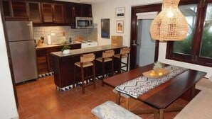 Una cocina con armarios de madera oscura, microondas, fregadero y comedor con un banco y sillas.