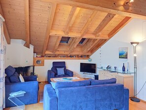 A living room with a high wooden ceiling, a sofa, a chair, a television, and a lamp.