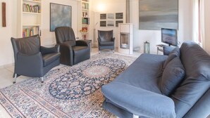 Un salon comprenant un canapé, deux fauteuils, une cheminée, un téléviseur et des étagères à livres.