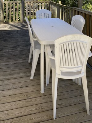 Une table en plastique blanc et quatre chaises sur une terrasse en bois.