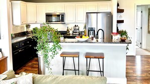 A modern kitchen with white cabinets, stainless steel appliances, and a central island with bar stools. - Eagle’s Roost - Views from the Top! (Banner Elk)