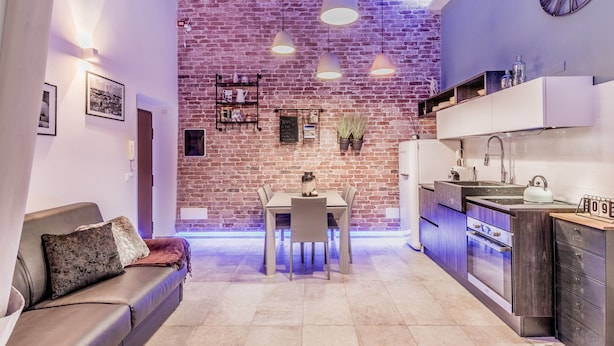 A modern kitchen with a brick wall, pendant lights, and a dining area with a table and chairs.