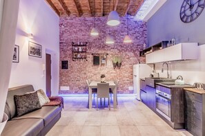 Een moderne keuken met een bakstenen muur, hanglampen en een eethoek met een tafel en stoelen.