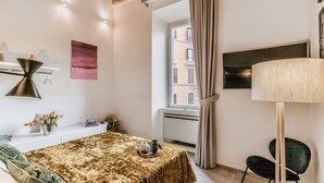 A bedroom with a bed, bedside table, lamp, and a view of the outside.