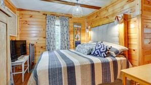 Ein Schlafzimmer einer Holzhütte mit einem Bett, einem Schreibtisch, einem Fernseher und einer Pendelleuchte.