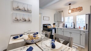 A dining area with a table set for two, a bowl of snacks, and wine glasses. There are nautical-themed paintings on the wall and a sign that reads "Lake Side." - Walk to Lake: Nautical Akron Cottage w/ Deck! (Akron)