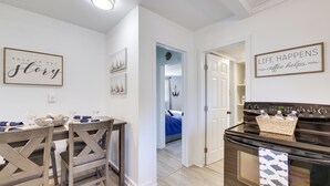 A modern kitchen with a dining table, chairs, and a stove. There are framed signs on the walls and a visible door leading to another room. - Walk to Lake: Nautical Akron Cottage w/ Deck! (Akron)