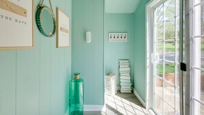 A room with teal walls, a large window, and a door. There are framed pictures on the wall, a stack of books, and a large bottle. - Walk to Lake: Nautical Akron Cottage w/ Deck! (Akron)