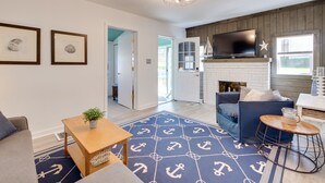 A living room with a blue rug, a fireplace, a TV, and a sofa. - Walk to Lake: Nautical Akron Cottage w/ Deck! (Akron)