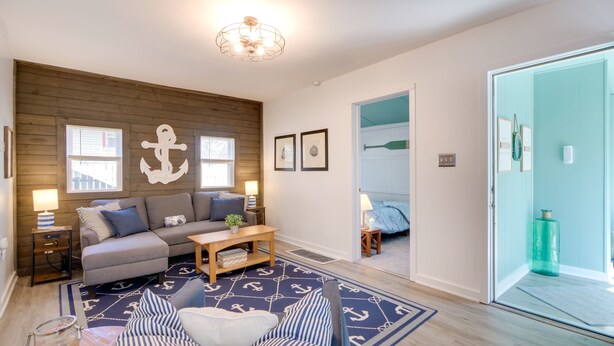 A living room with a grey sofa, a wooden accent wall, and a nautical-themed rug. - Walk to Lake: Nautical Akron Cottage w/ Deck! (Akron)