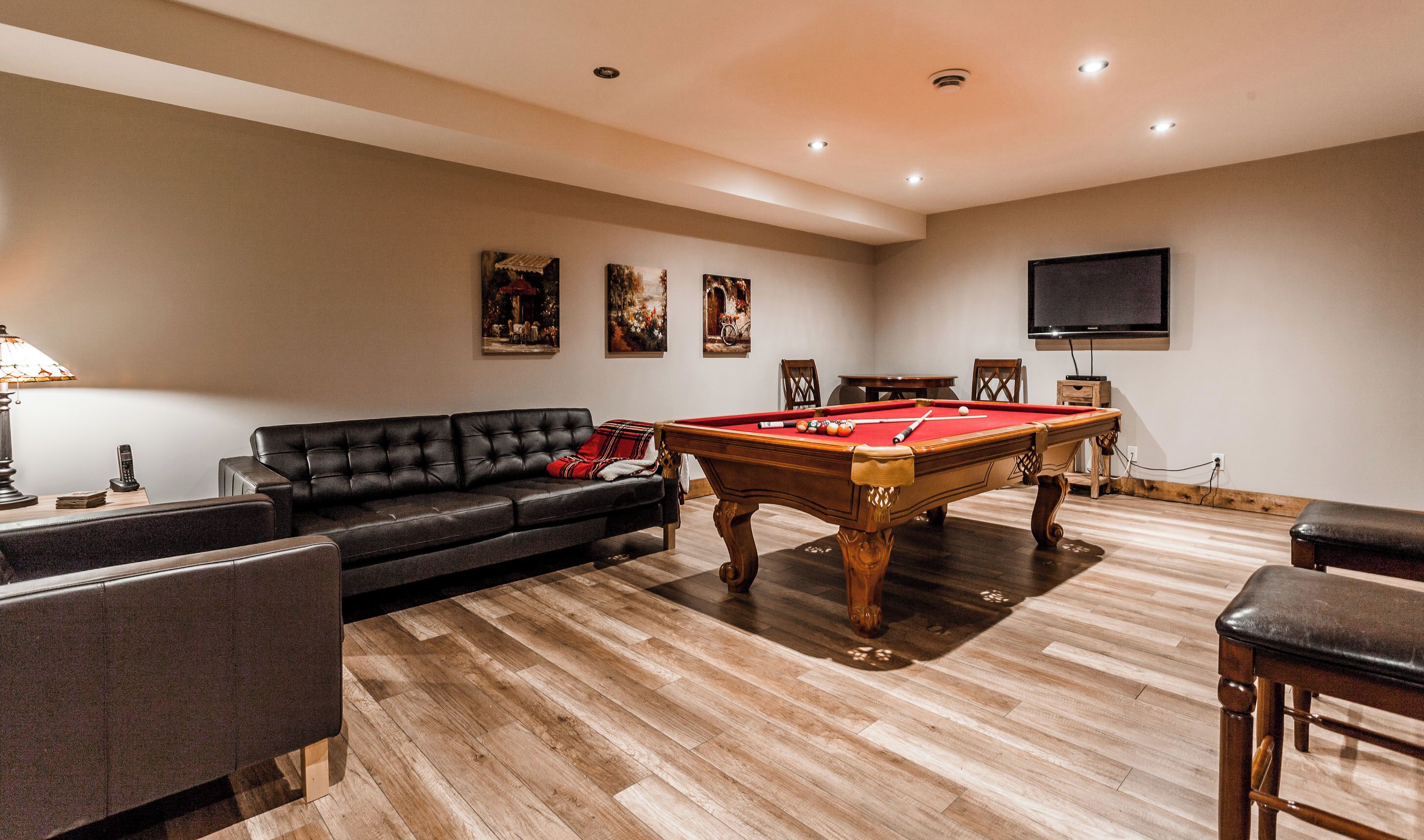 Une pièce comprenant une table de billard, un canapé, un téléviseur et des œuvres d’art accrochées au mur.