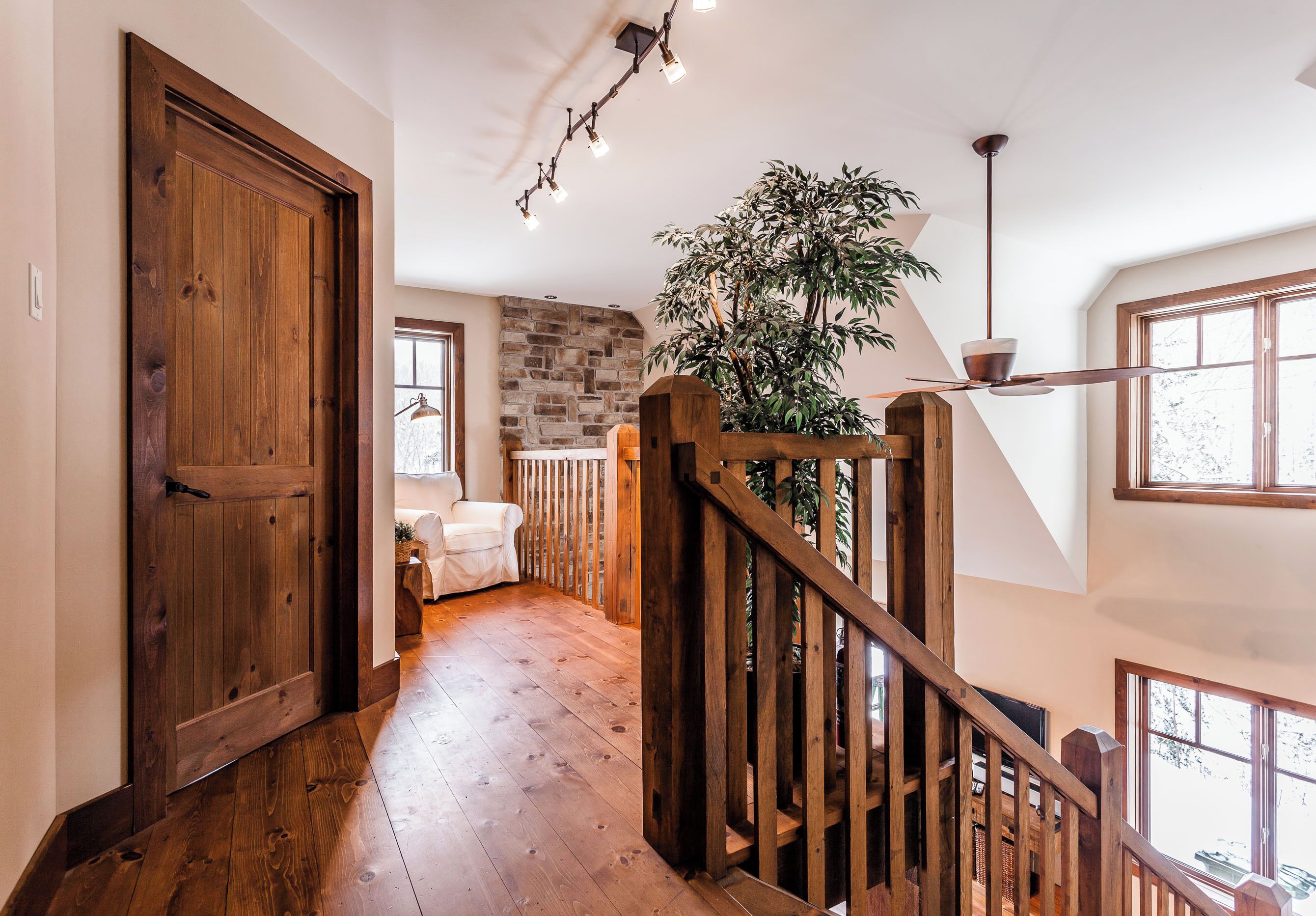 A wooden staircase leading to a second floor, a large potted plant, and a stone wall.