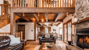 Un espacio habitable amplio con chimenea, vigas de madera, un sofá de cuero y un comedor al fondo.
