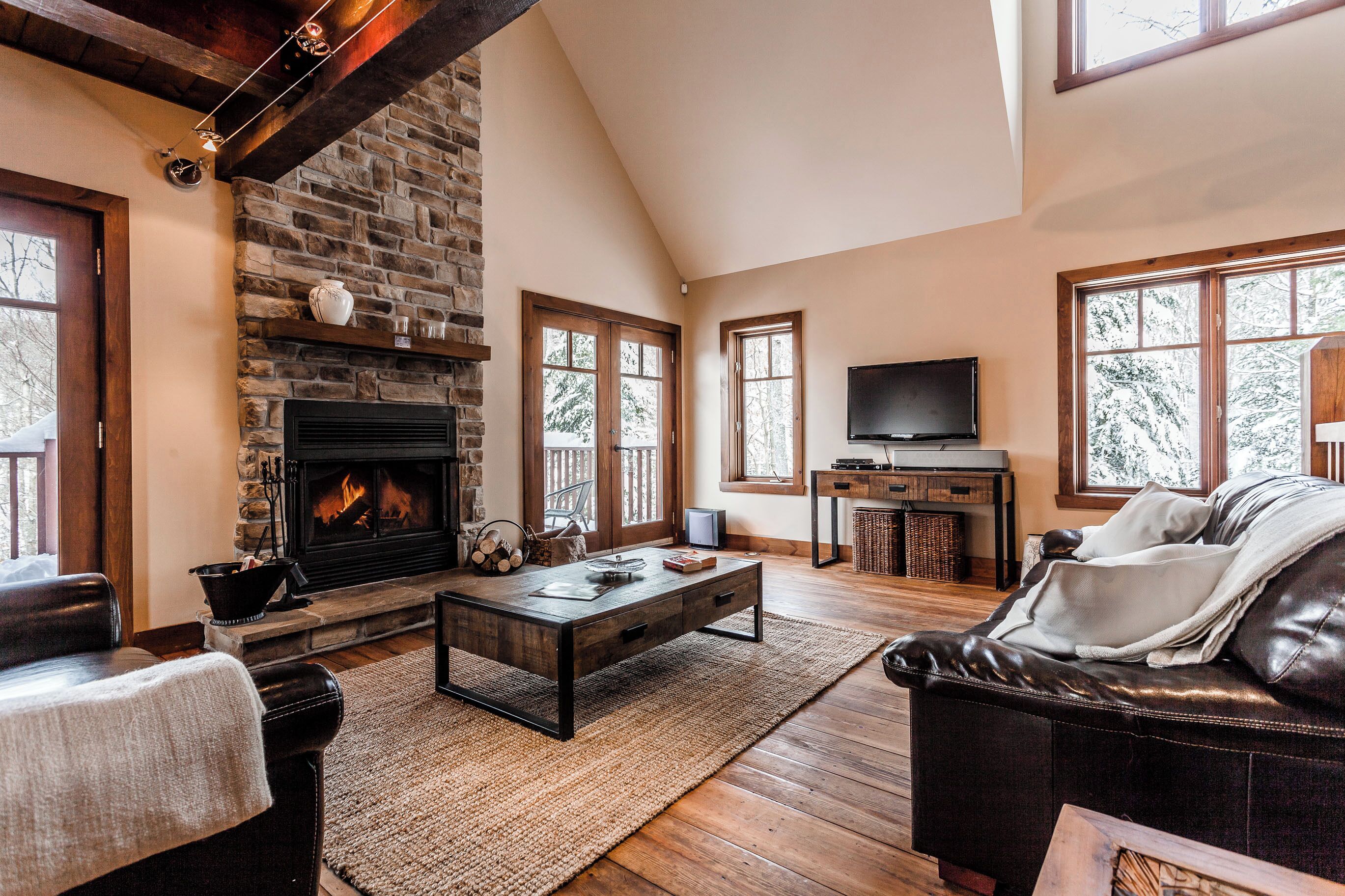 Una sala de estar acogedora con chimenea, muebles de cuero y ventanas amplias.