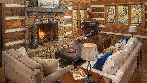 L’intérieur d’une cabane en rondins, avec une cheminée en pierre, des murs en bois, un lustre et un coin salon confortable.
