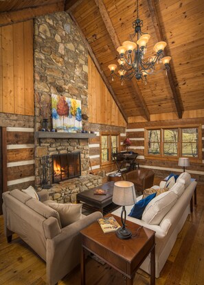A log cabin interior with a stone fireplace, wooden walls, a chandelier, and a cozy seating area. - Reconnect With Nature at The Briar Patch (Sugar Grove)
