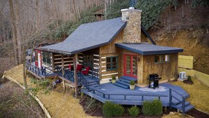 Une cabane en rondins avec une véranda, une cheminée et une terrasse.