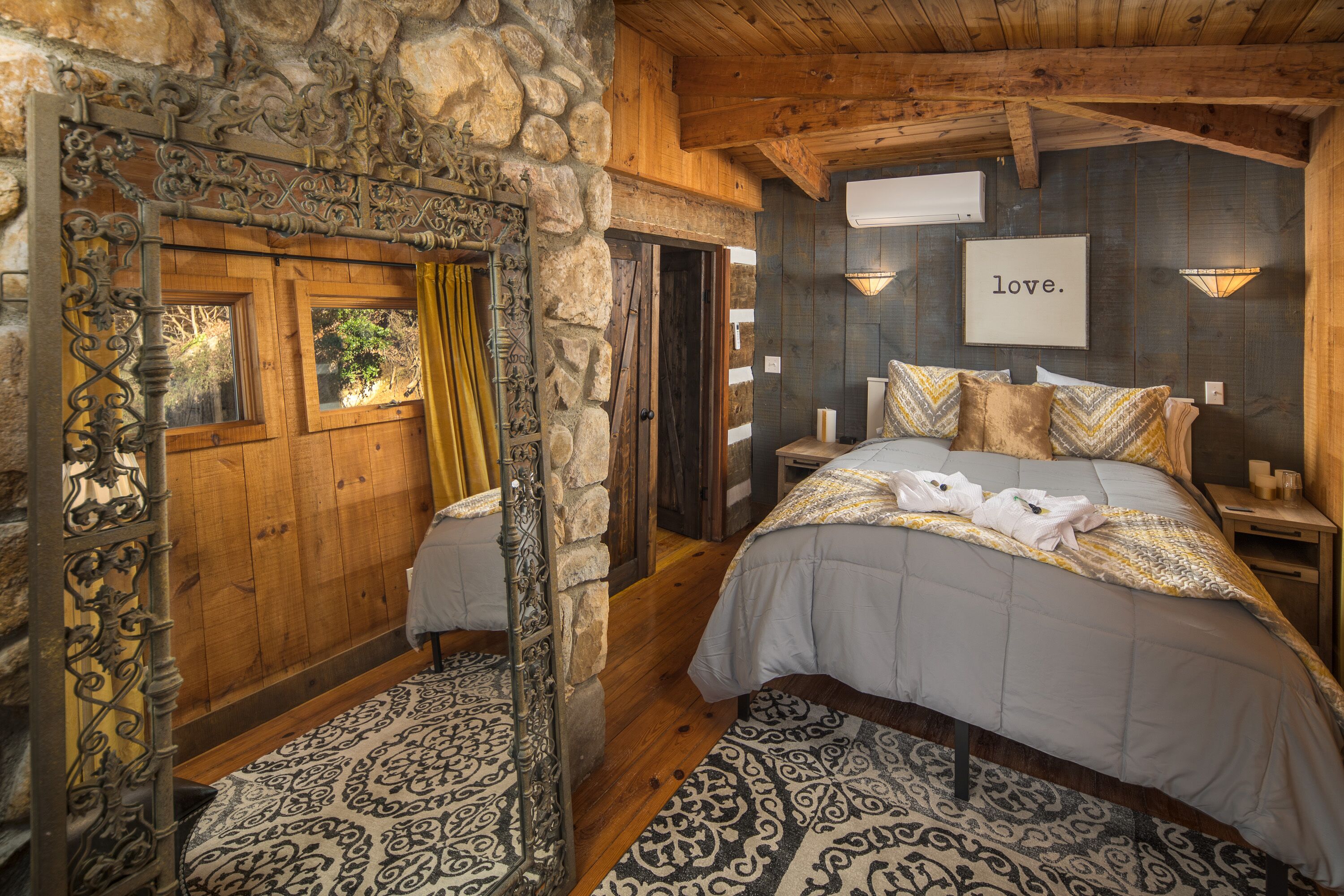 A cozy bedroom with a large bed, a stone wall, and a wooden ceiling.