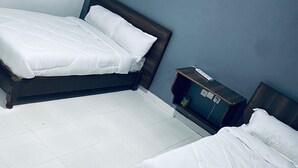 A hotel room with two single beds, a small bedside table, and a nightstand. - Dad's Place (Karatina)