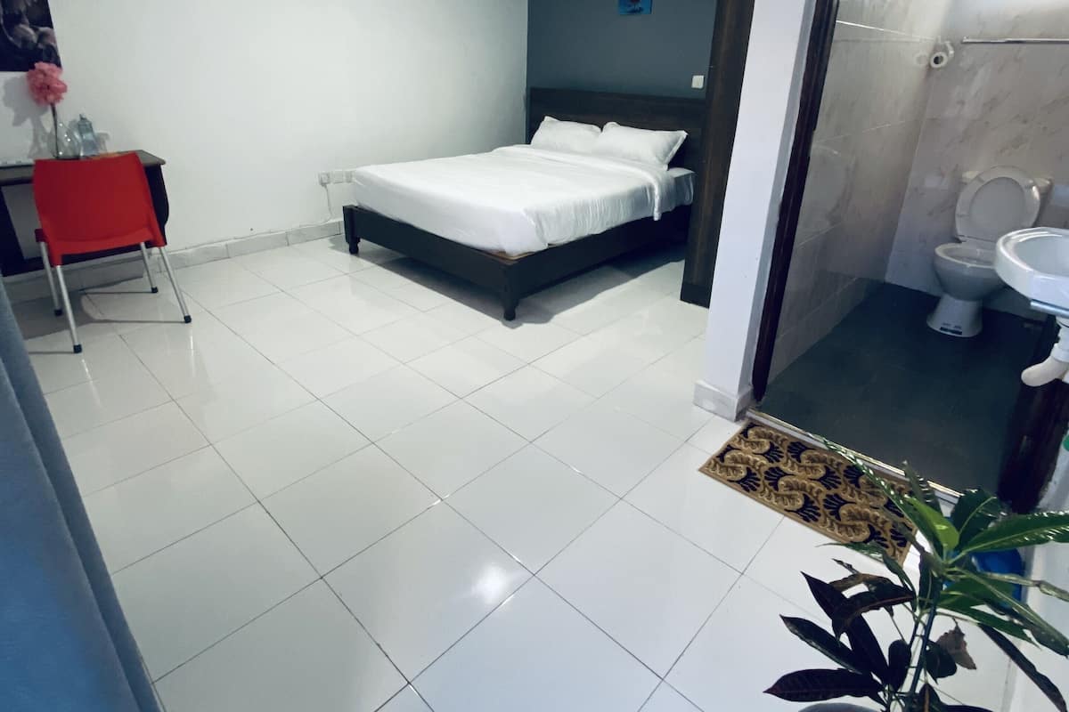 A modern hotel room with a bed, a desk, a chair, and a potted plant.