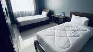 Ein Hotelzimmer mit zwei Betten, einem Nachttisch und einem Fenster mit Vorhängen.