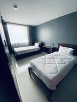 Una habitación de hotel con dos camas, una mesita de noche y un ventanal con cortinas.