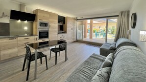A modern kitchen with built-in appliances, a dining area with a glass table, and a living room with a sofa and a sliding glass door to a patio. - Nice studio with balcony located in Fréjus. (Fréjus)