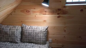 A wooden ceiling with a hanging lamp, a patterned sofa, and a window with a decorative grille. - Charming cabin overlooking river Smoky mountains (Chuckey)