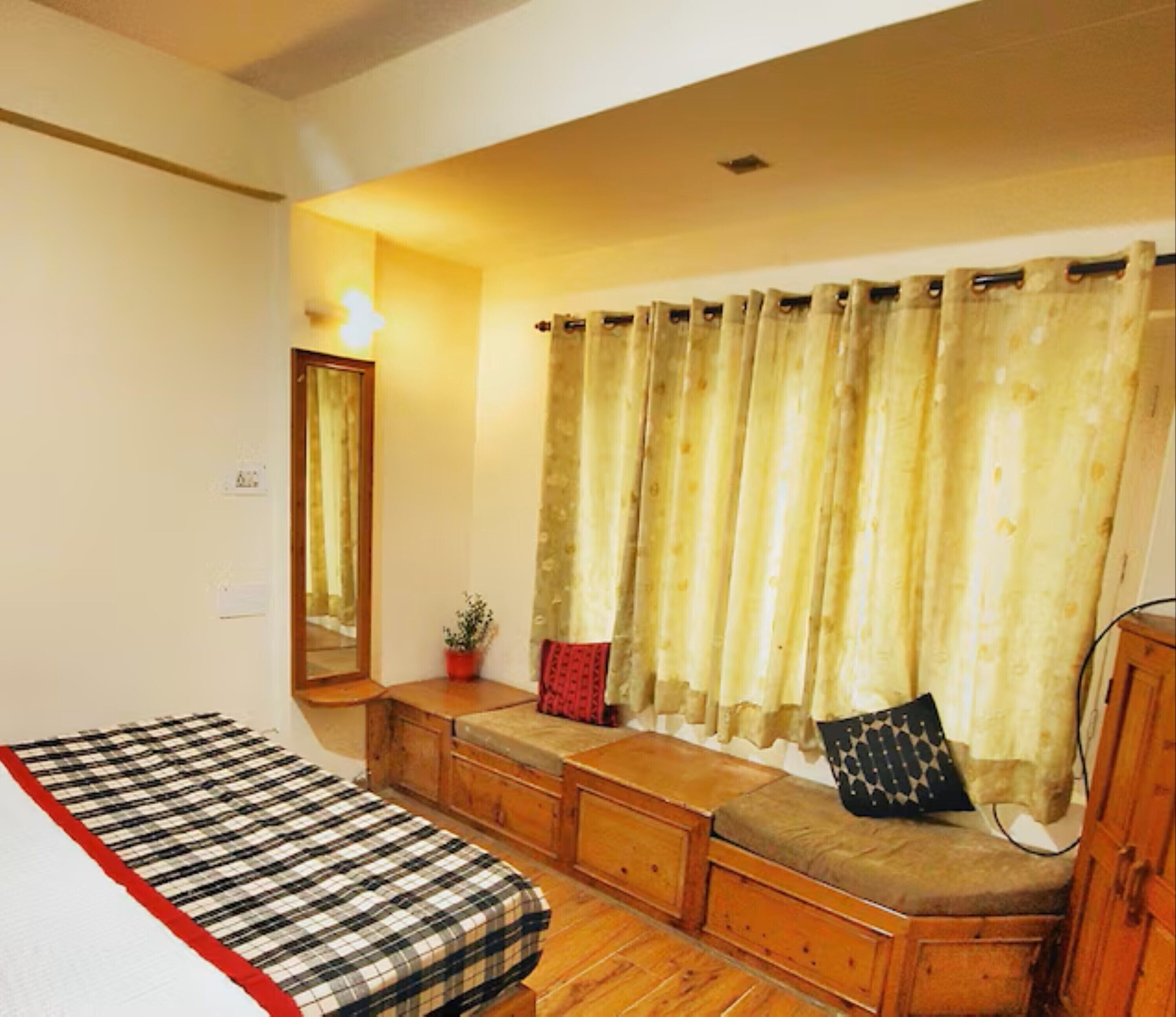 Une chambre à coucher comprenant un lit, un banc, un miroir, une fenêtre avec des rideaux et une armoire.
