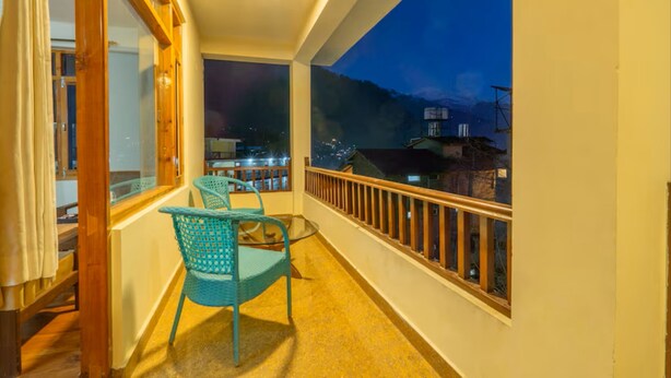 A balcony with a view of a cityscape at night, featuring a wooden railing and a glass door leading to an interior space.
