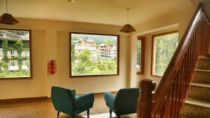 A room with a large window offering a view of buildings and greenery. There are two chairs and a fire extinguisher on the wall.