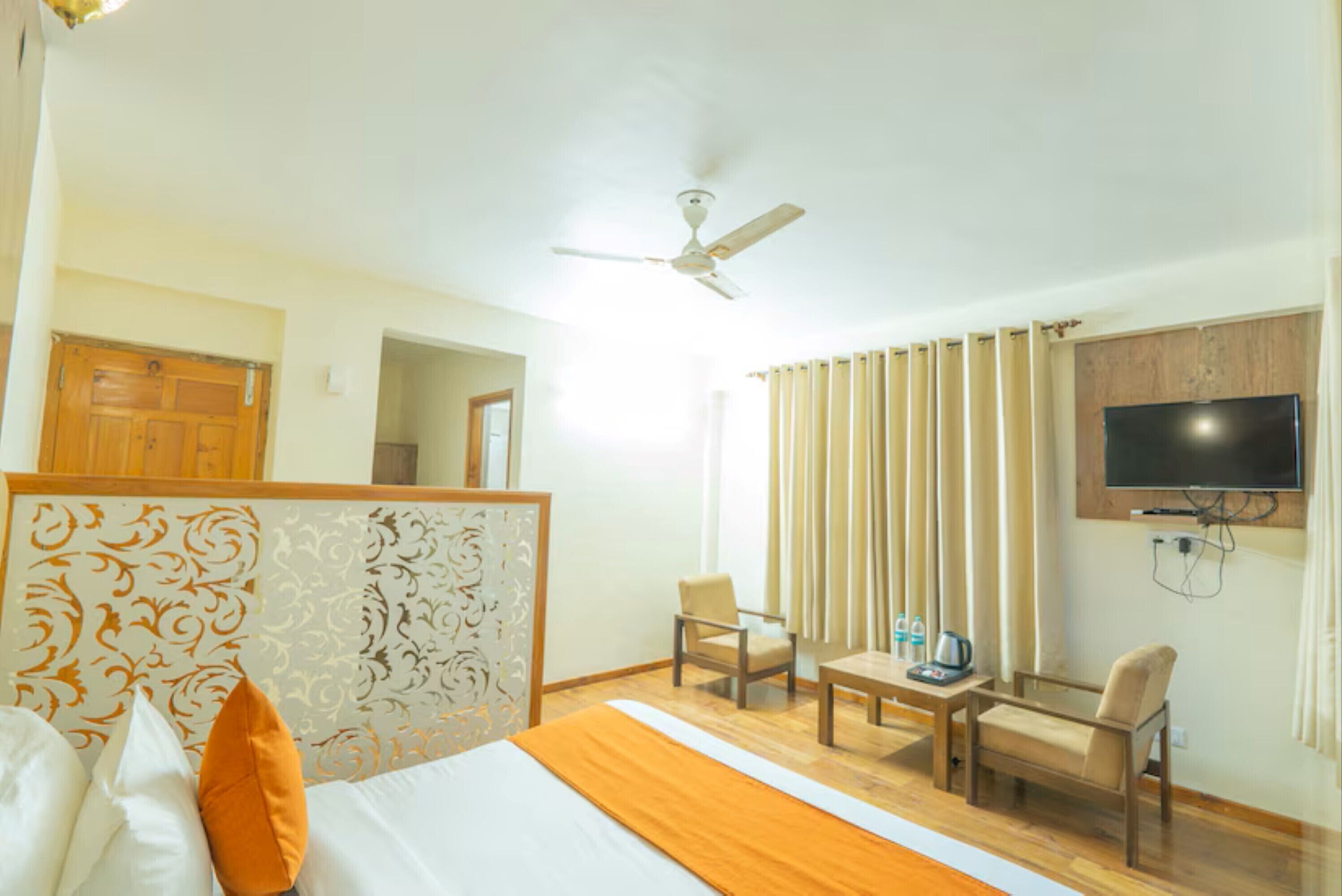 A hotel room with a bed, a desk, two chairs, a television, and a ceiling fan.