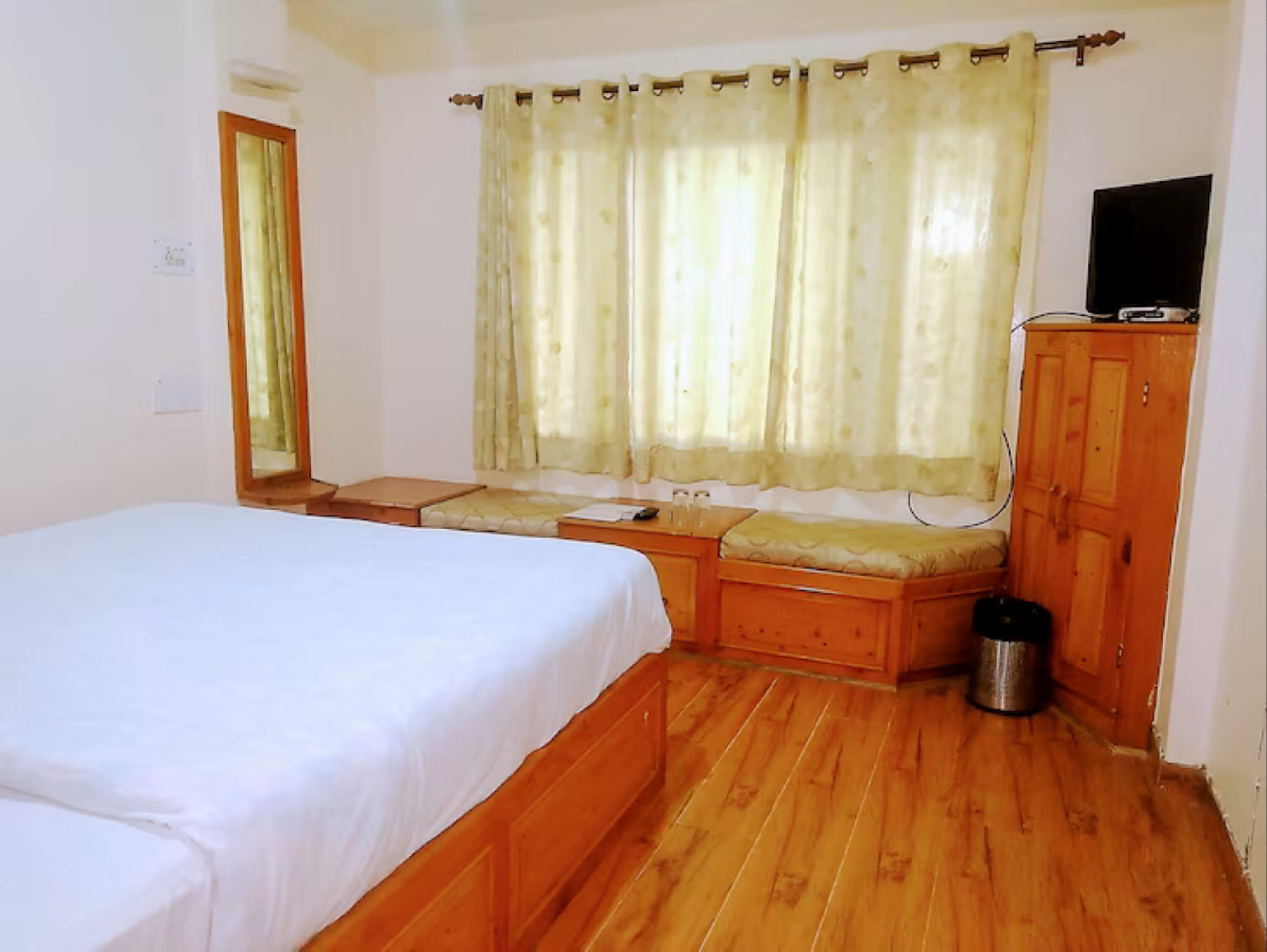 Una stanza con un letto, una panca di legno, un tavolino, una televisione e un armadio.