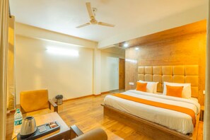 A hotel room with a large bed, a desk with a kettle, and a chair.