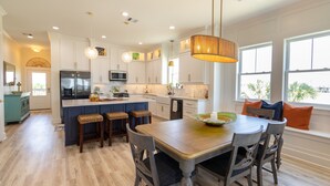 Een moderne keuken met witte kastjes, een centraal eiland en een eethoek met houten stoelen en een tafel.
