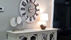 A living room with a white console table, a large wall clock, decorative plates, and a lamp. - Celebrate Branson (Branson)