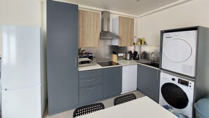 A compact kitchen with a built-in washing machine, a refrigerator, and a dining area with a table and chairs. - Appartement 6 Personnes Berck, à 400 Mètres de la Plage! (Berck)