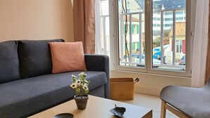 A modern living room with a grey sofa, a wooden coffee table, a potted plant, and a view of buildings through large windows. - Appartement 6 Personnes Berck, à 400 Mètres de la Plage! (Berck)