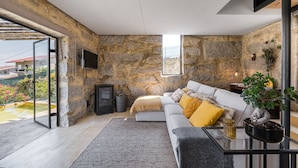 A modern living room with a stone wall, a sofa with yellow cushions, a glass coffee table, and a potted plant. - Lemon House - Valpendre (Valpedre)