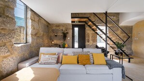A modern living room with a stone wall, a sofa with patterned cushions, and a staircase. - Lemon House - Valpendre (Valpedre)