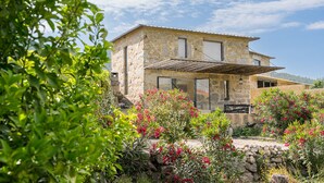 A stone house with a covered patio, surrounded by lush greenery and flowering plants. - Lemon House - Valpendre (Valpedre)