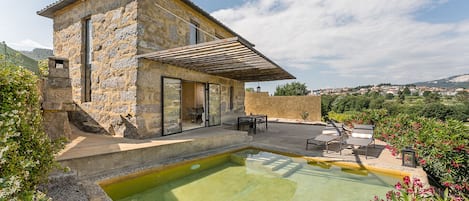 A stone building with a pool, outdoor seating, and a view of the landscape.